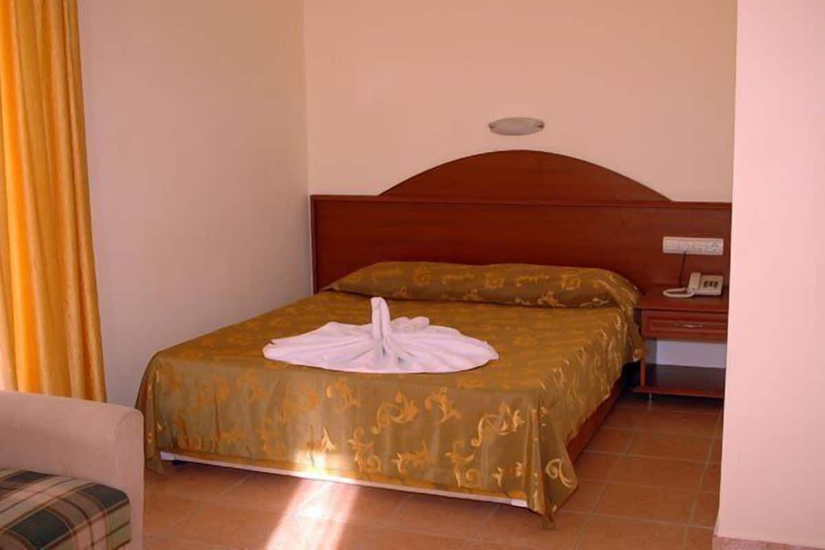 A hotel room with a bed, a bedside table with a phone, and a curtain.