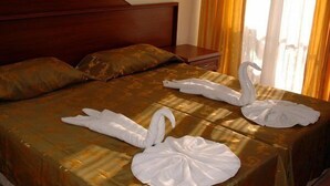 A hotel room with a large bed, two pillows, a wooden headboard, a nightstand, and a window with curtains. - Inside Hotel (Manavgat)