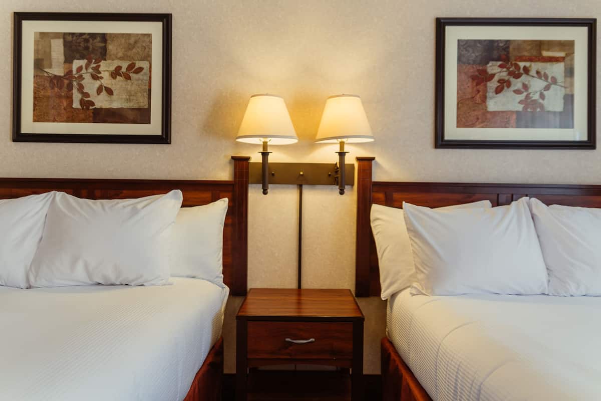 A hotel room with two beds, a nightstand, and two wall-mounted lamps.