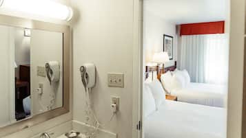 A hotel room with a bathroom, a bed, and a nightstand with a lamp.