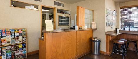 A reception area with a wooden desk, a bulletin board, a trash can, and a seating area with stools.