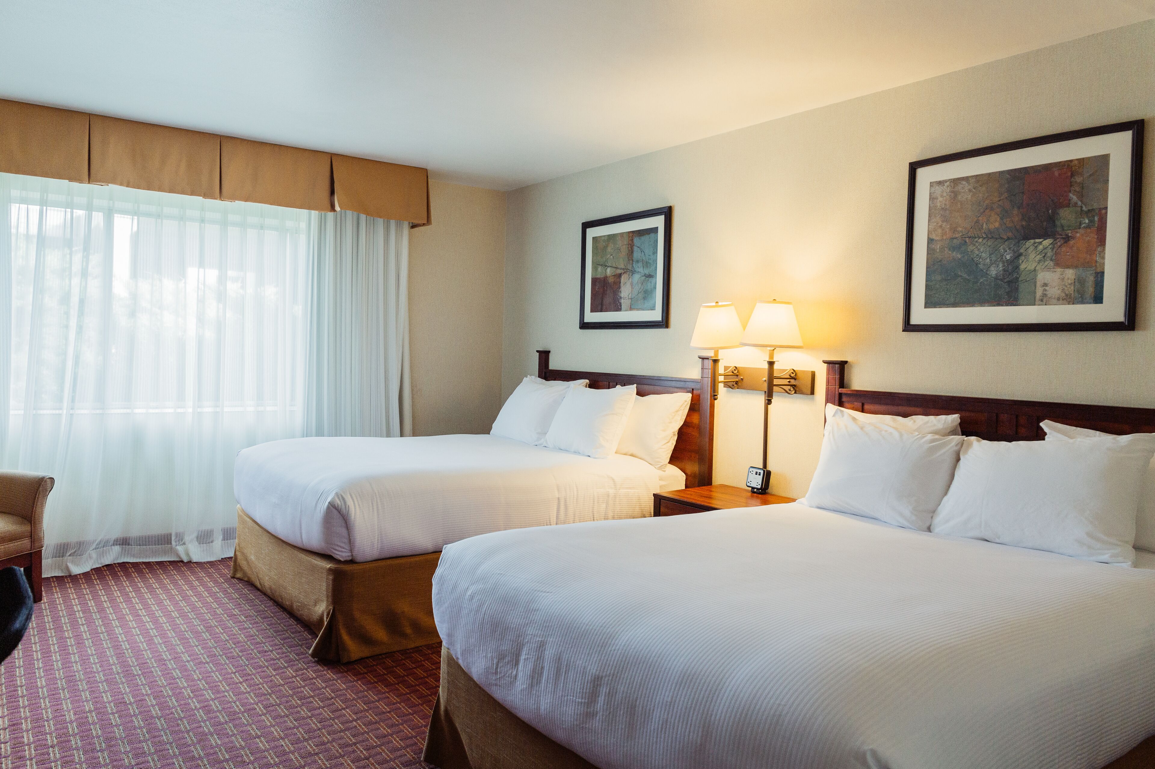 A hotel room with two beds, a desk, a chair, and two lamps.