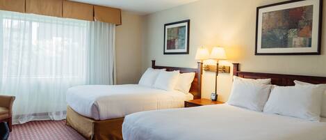 A hotel room with two beds, a desk, a chair, and two lamps.