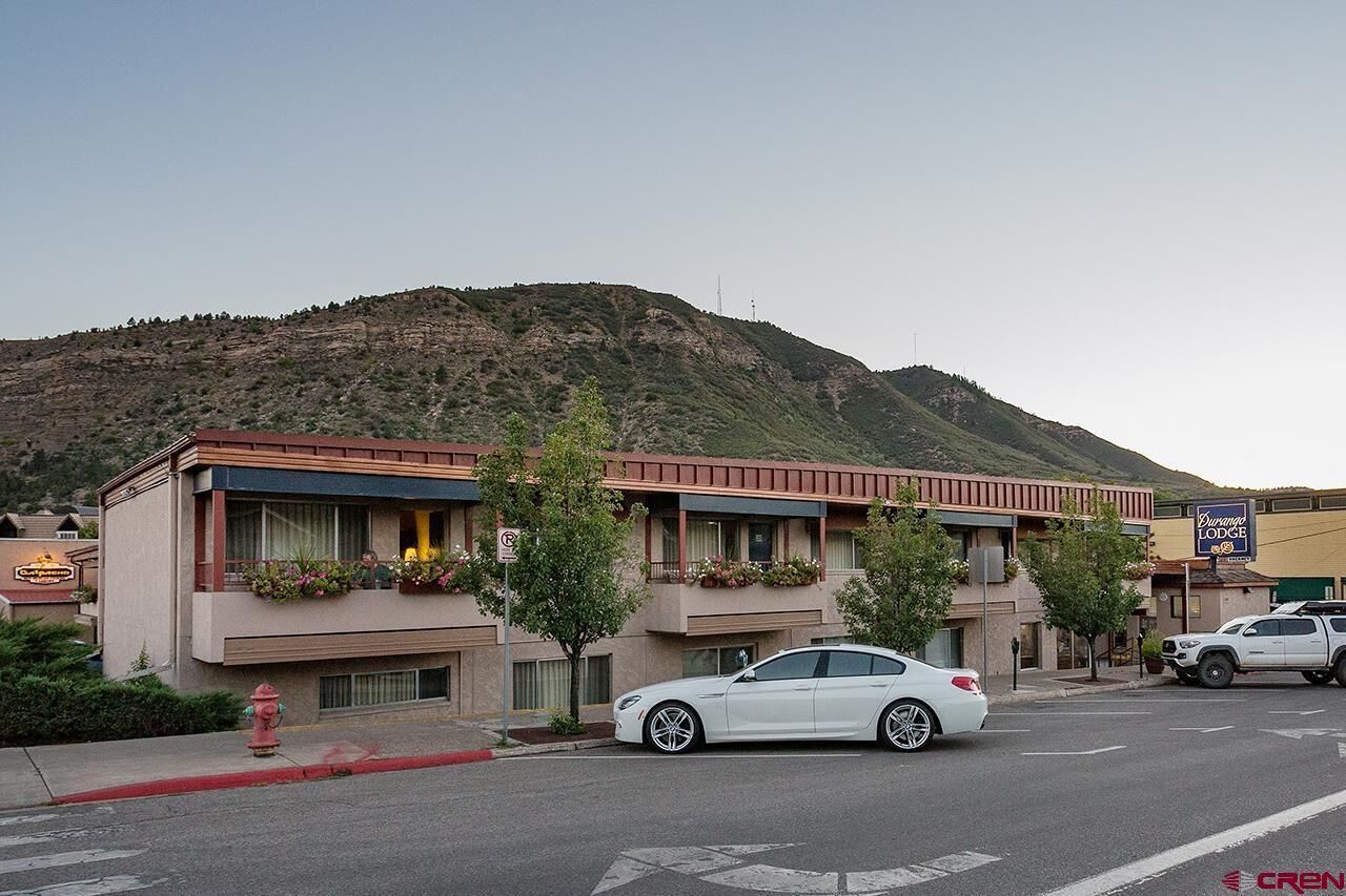A motel with a mountain backdrop, a white car parked in front, and a fire hydrant on the sidewalk.