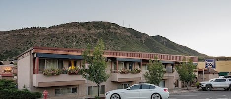 A motel with a mountain backdrop, a white car parked in front, and a fire hydrant on the sidewalk.