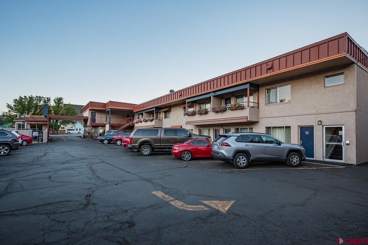 Un estacionamiento con varios coches aparcados frente a un motel de varias plantas y balcones.