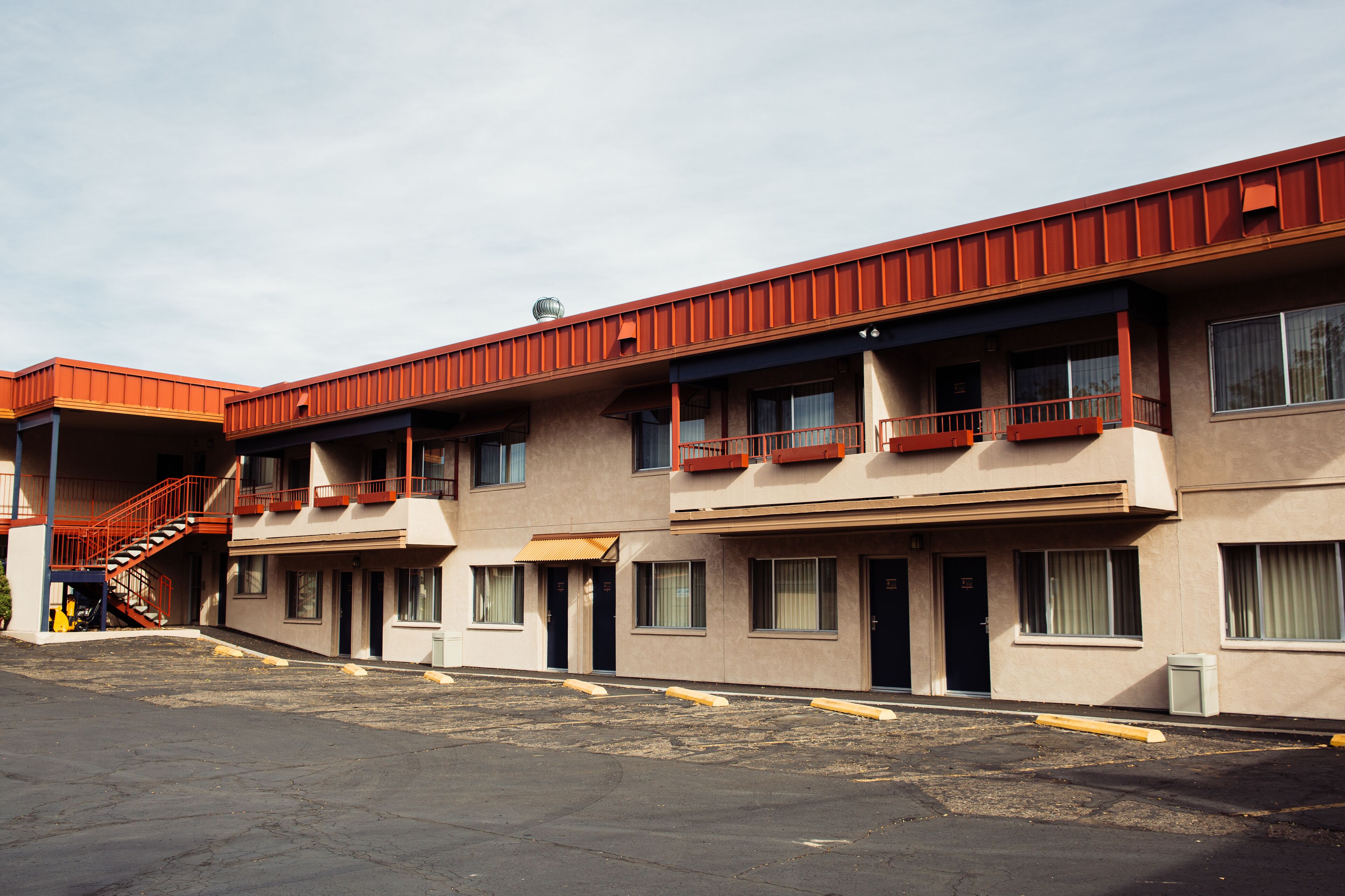 A row of motel buildings with balconies and a parking lot in front.