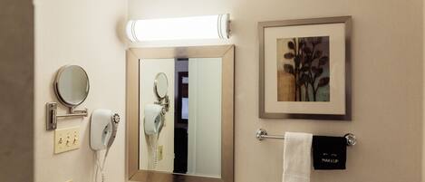 A bathroom with a large mirror, a hairdryer, a telephone, and a framed picture on the wall.