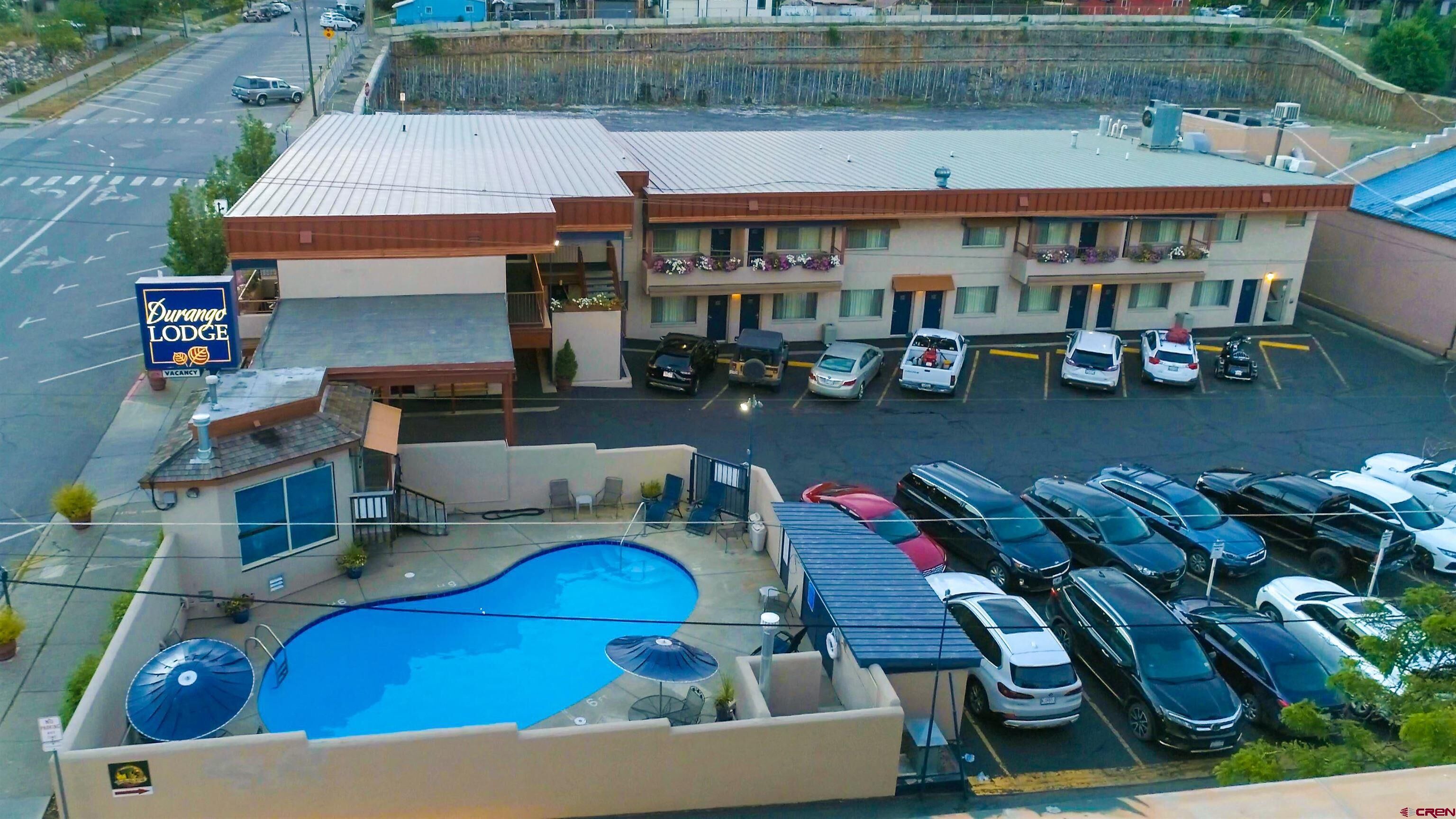 A motel with a swimming pool, multiple parking spaces, and a sign indicating vacancy.