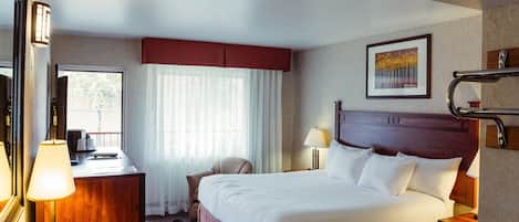 A hotel room with a bed, bedside tables, a desk, a chair, a window with curtains, and a painting on the wall.