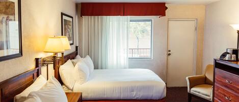 Habitació d'hotel amb dos llits, una cadira, un taulell i una finestra amb cortines.