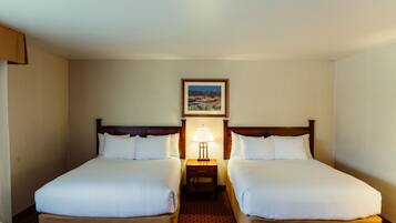 A hotel room with two single beds, a nightstand with a lamp, and a framed picture on the wall.