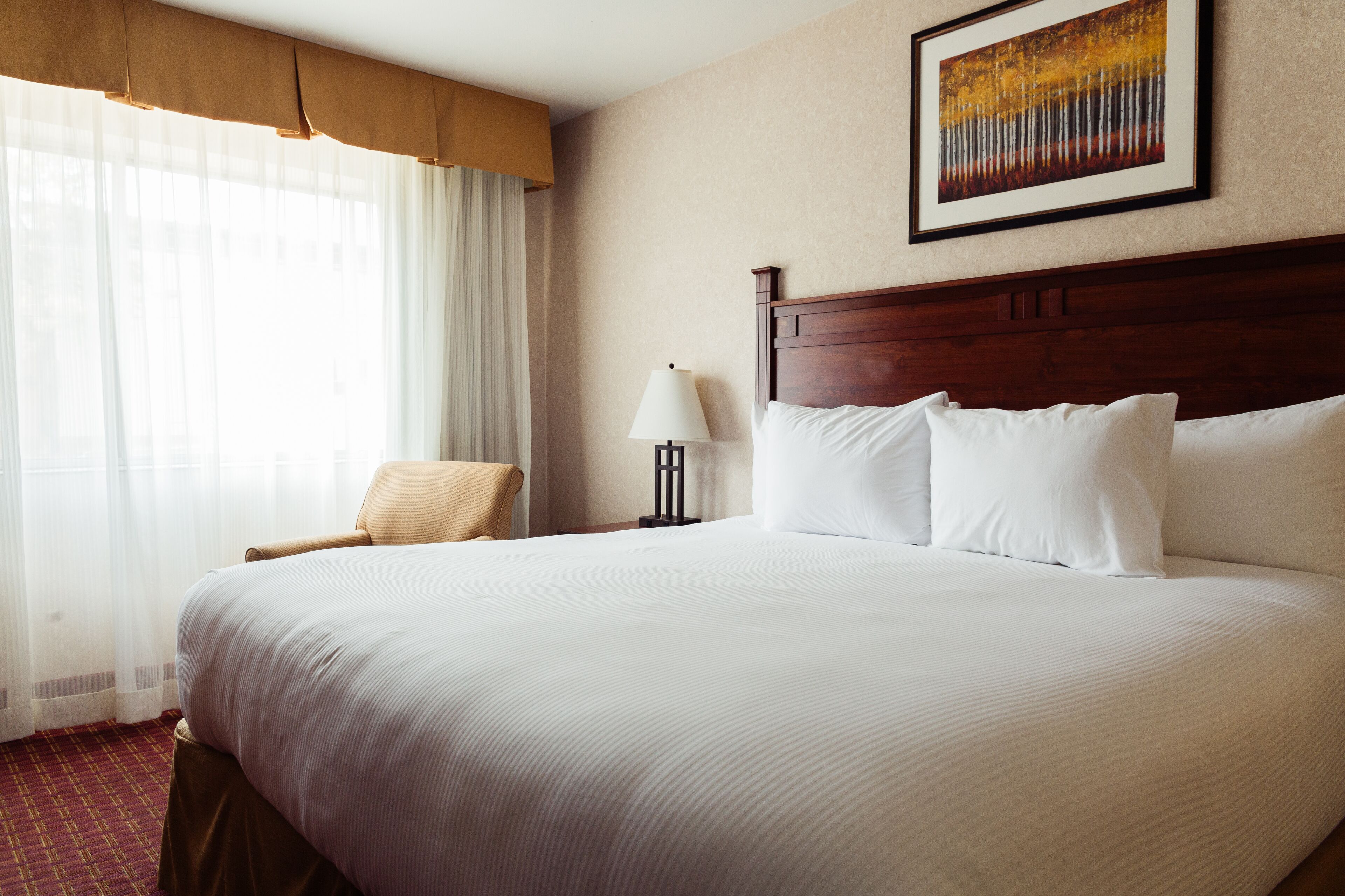 Een hotelkamer met een groot bed, een stoel, een lamp en een schilderij aan de muur.