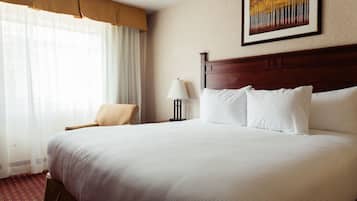 Een hotelkamer met een groot bed, een stoel, een lamp en een schilderij aan de muur.