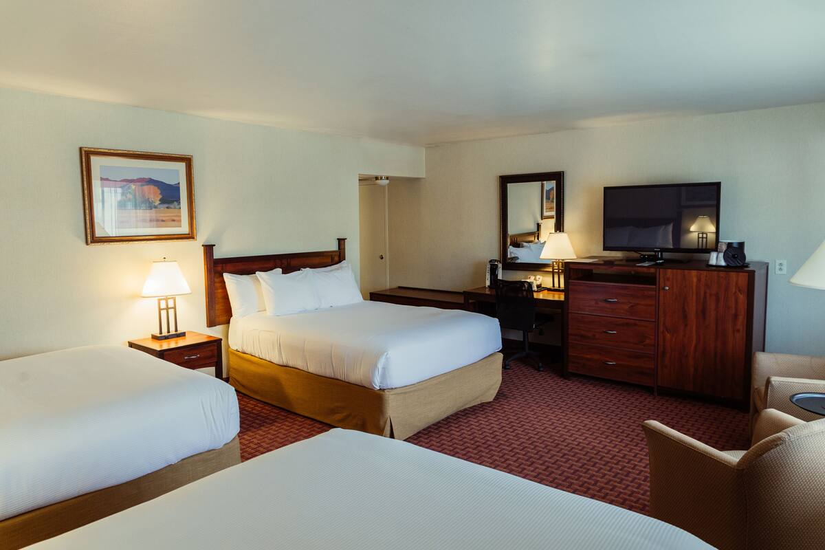 A hotel room with two beds, a desk, a television, and a mirror.