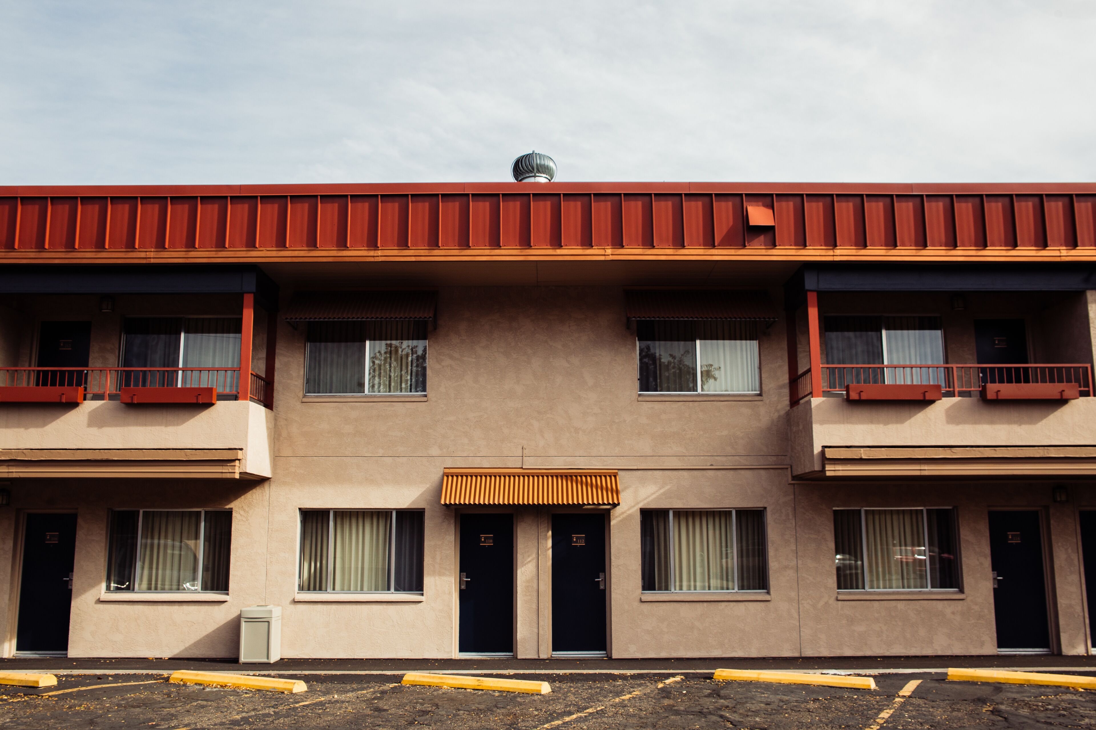 A multi-story building with a flat roof, two balconies on each floor, and a central entrance with an awning.