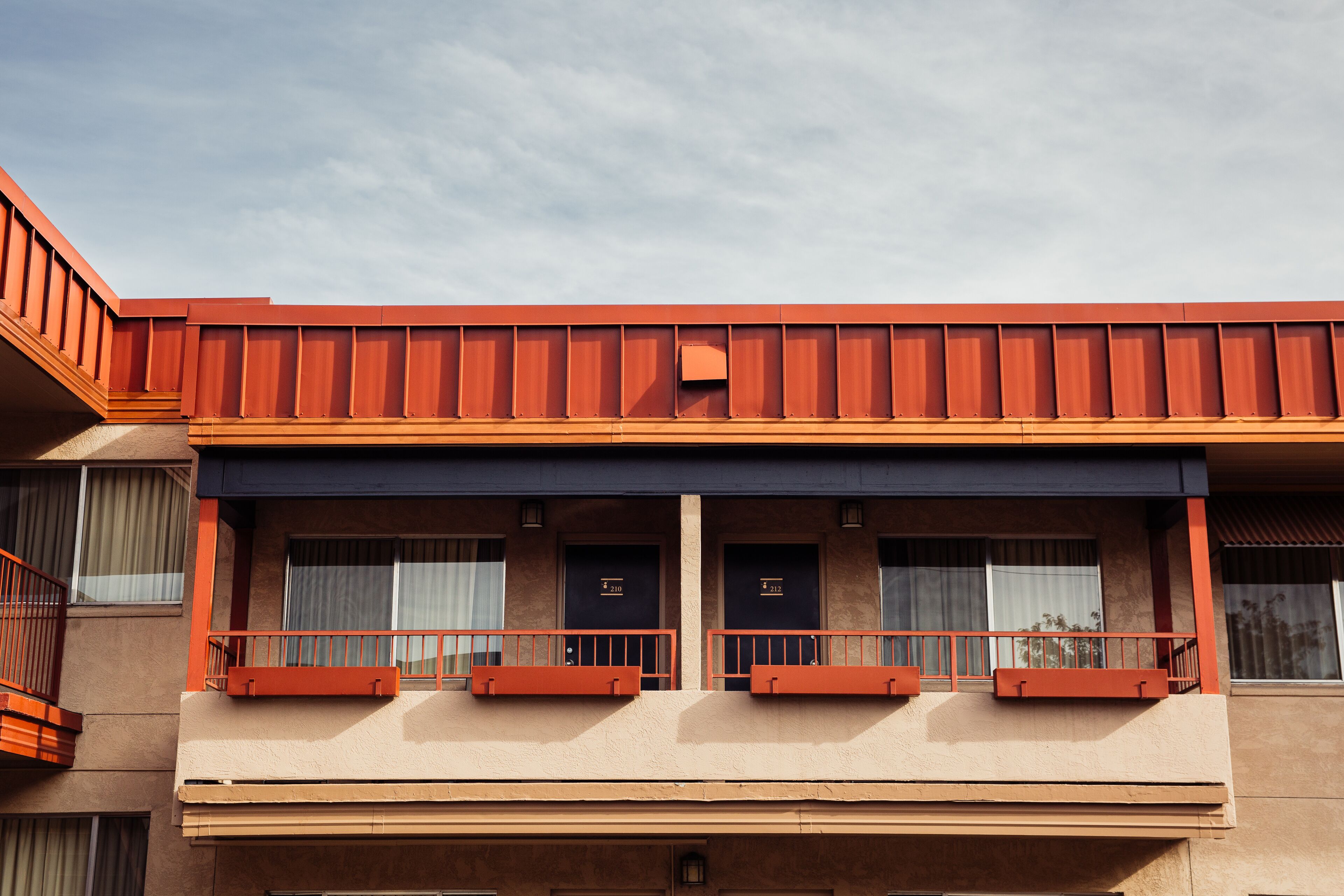 A hotel with a red roof, two-story structure, and balconies with orange railings.