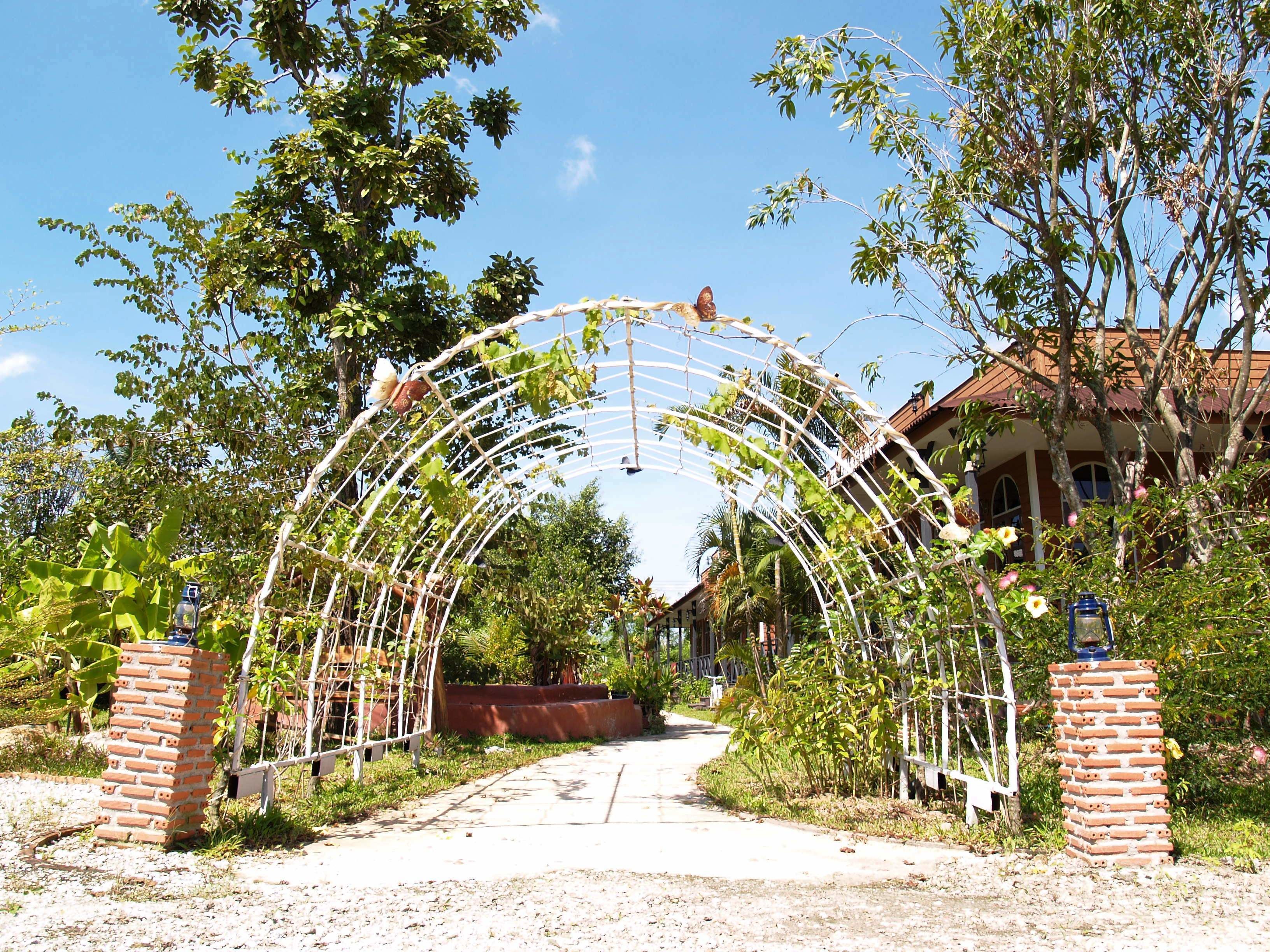 A brick archway leading to a building with a red roof, surrounded by greenery.