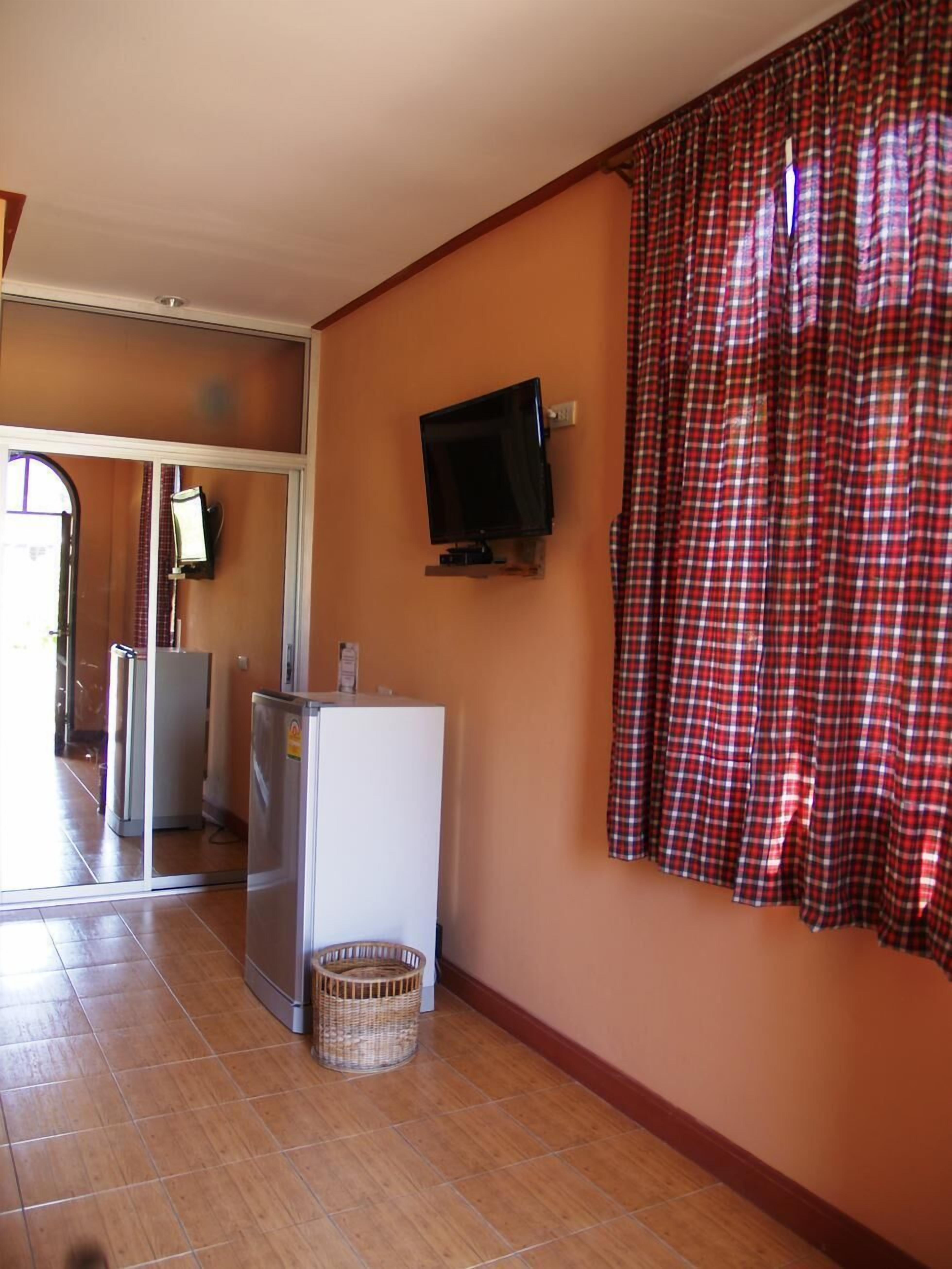 A compact living space with a television mounted on the wall, a refrigerator, and a wicker basket on the floor.