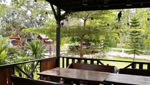 An outdoor wooden deck with benches and tables, surrounded by lush greenery and trees. - Cowboy Farm Resort Pattaya (Bang Lamung)