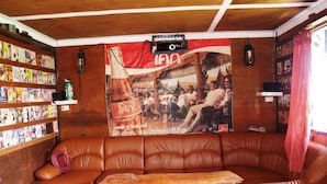 A cozy lounge area with a leather sofa, a wooden coffee table, and a wall adorned with a large poster and a shelf of magazines. - Cowboy Farm Resort Pattaya (Bang Lamung)