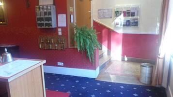 Een hotel lobby met een receptiebalie, een sleutelrek aan de muur, een potplant en een trap naar een andere verdieping.