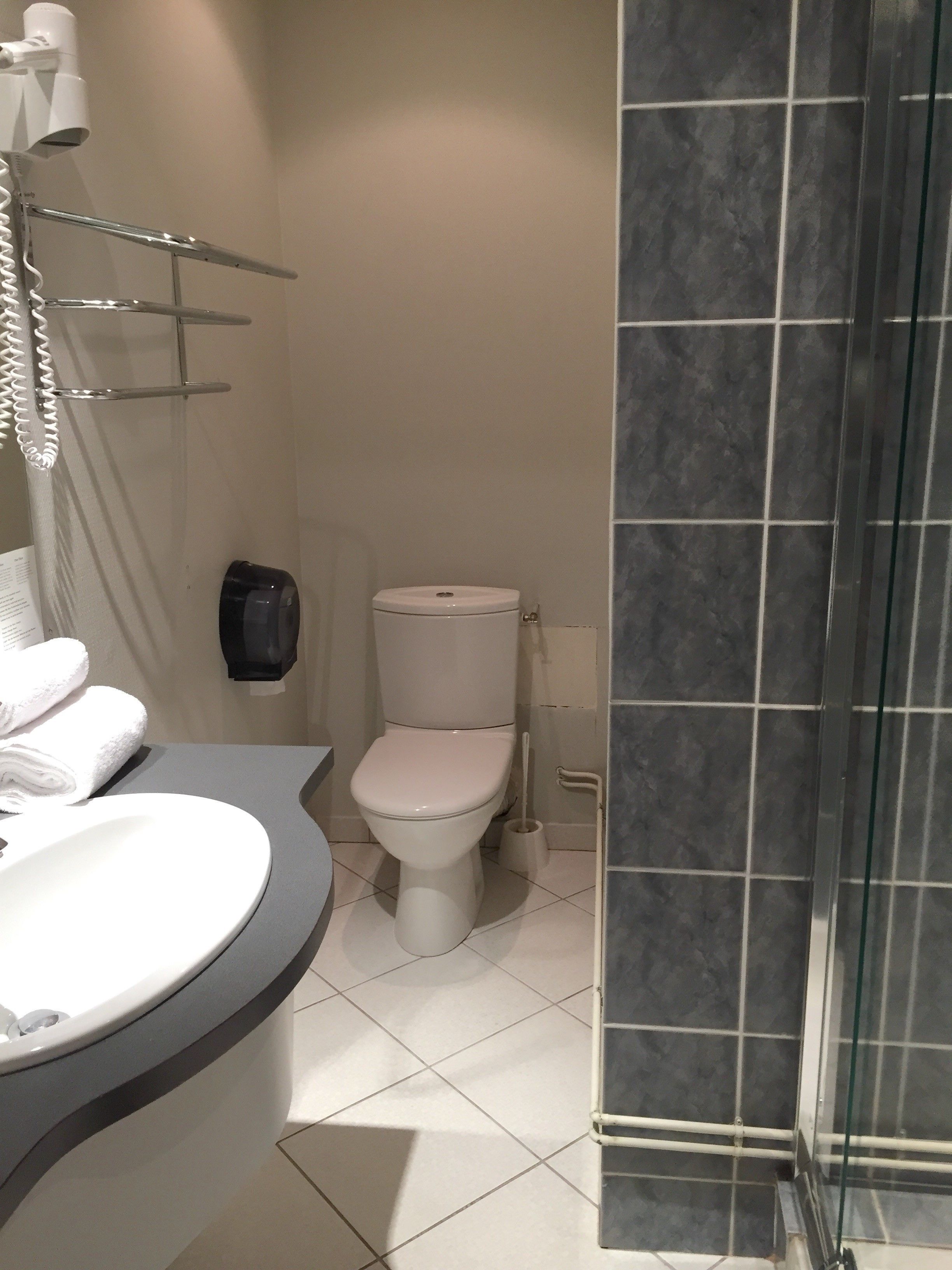 Casa de banho com sanita branca, lavatório com espelho e zona de duche com porta de vidro.