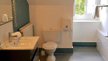 A bathroom with a white toilet, a sink with a mirror, and a window providing natural light.