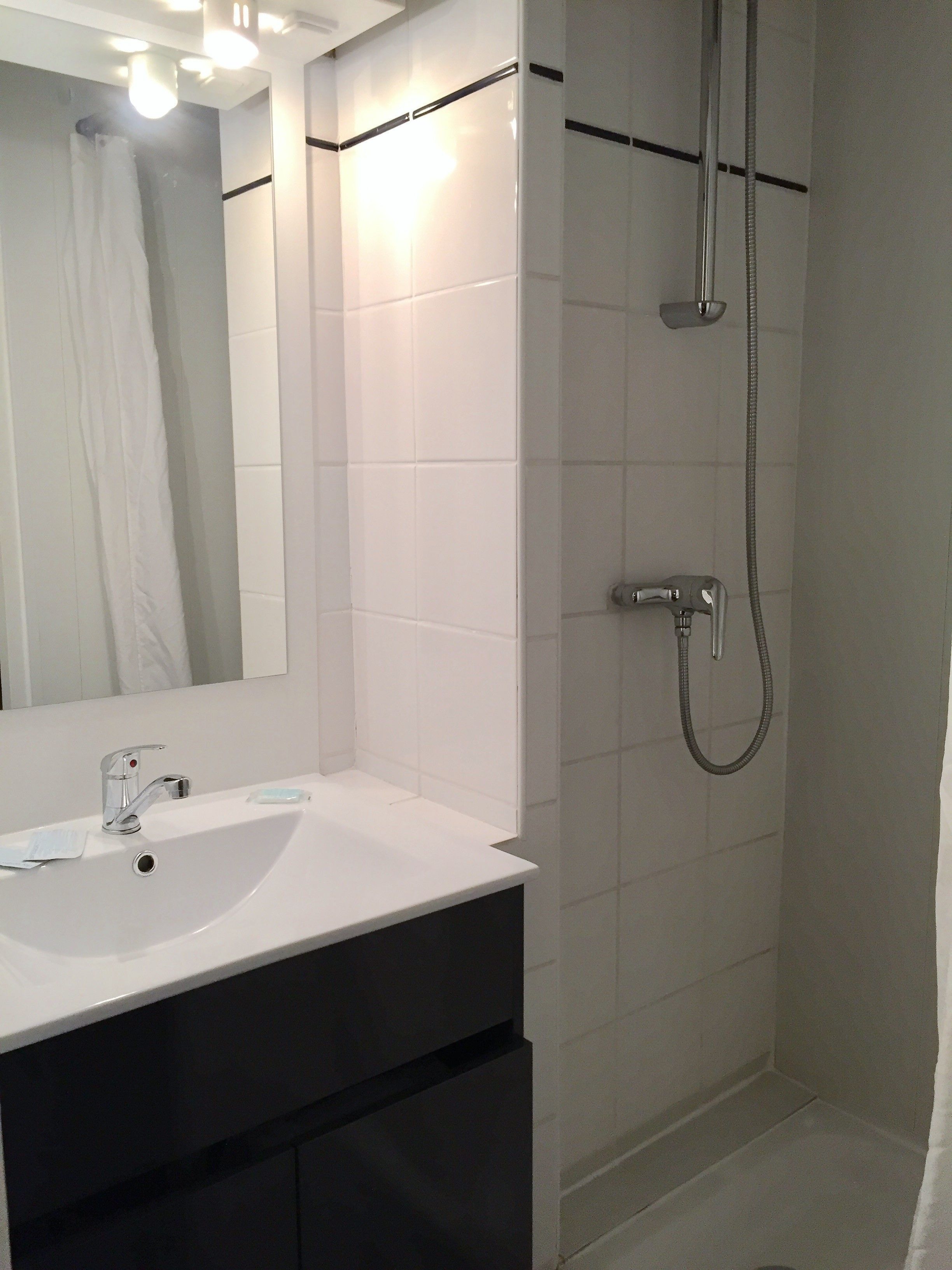 Casa de banho com lavatório branco, espelho e chuveiro com chuveiro manual.