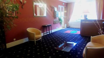 Habitación de hotel con pared roja, alfombra azul estampada, una silla, una mesita y un espejo.