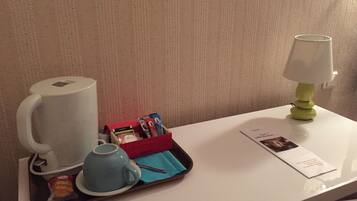 A hotel room with a coffee maker, a tray with tea bags and a spoon, a lamp, and a menu on the table.