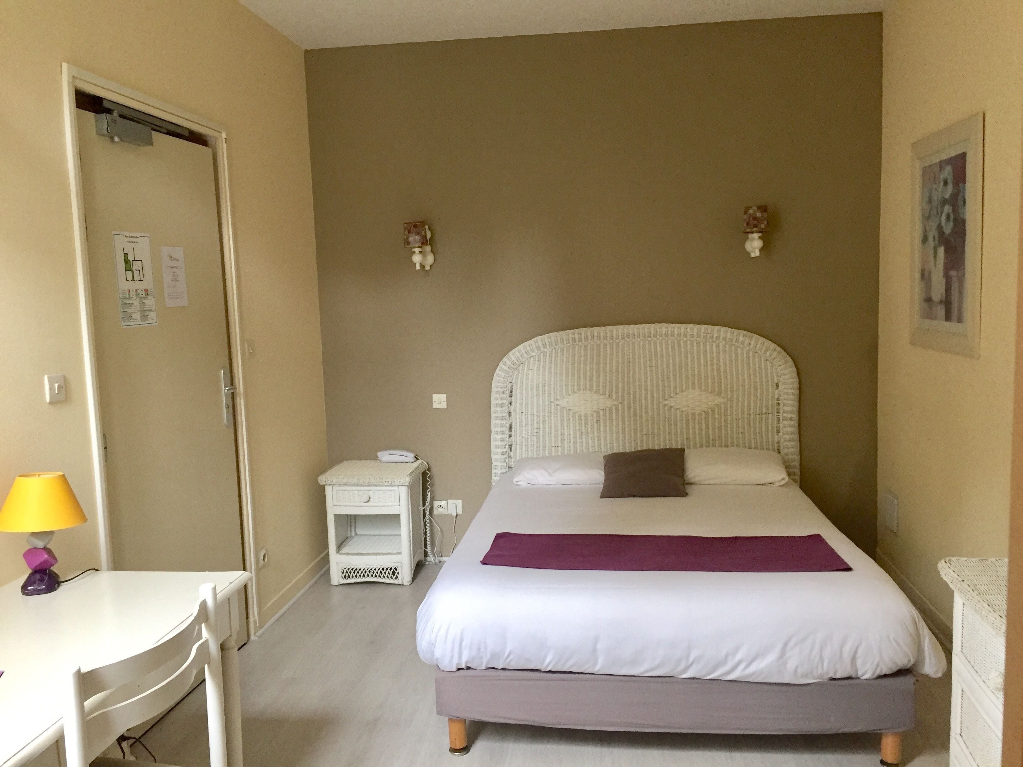 A bedroom with a bed, a desk, a chair, a nightstand, and a lamp.