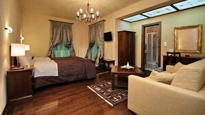 Habitación de hotel con cama, sofá, escritorio, candelabro, cortinas, televisor y espejo.