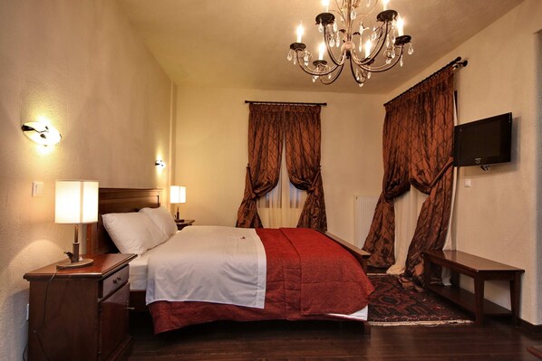 A hotel room with a bed, bedside lamps, a TV, and a chandelier. - Aiora Luxury Suites (Gortynia)