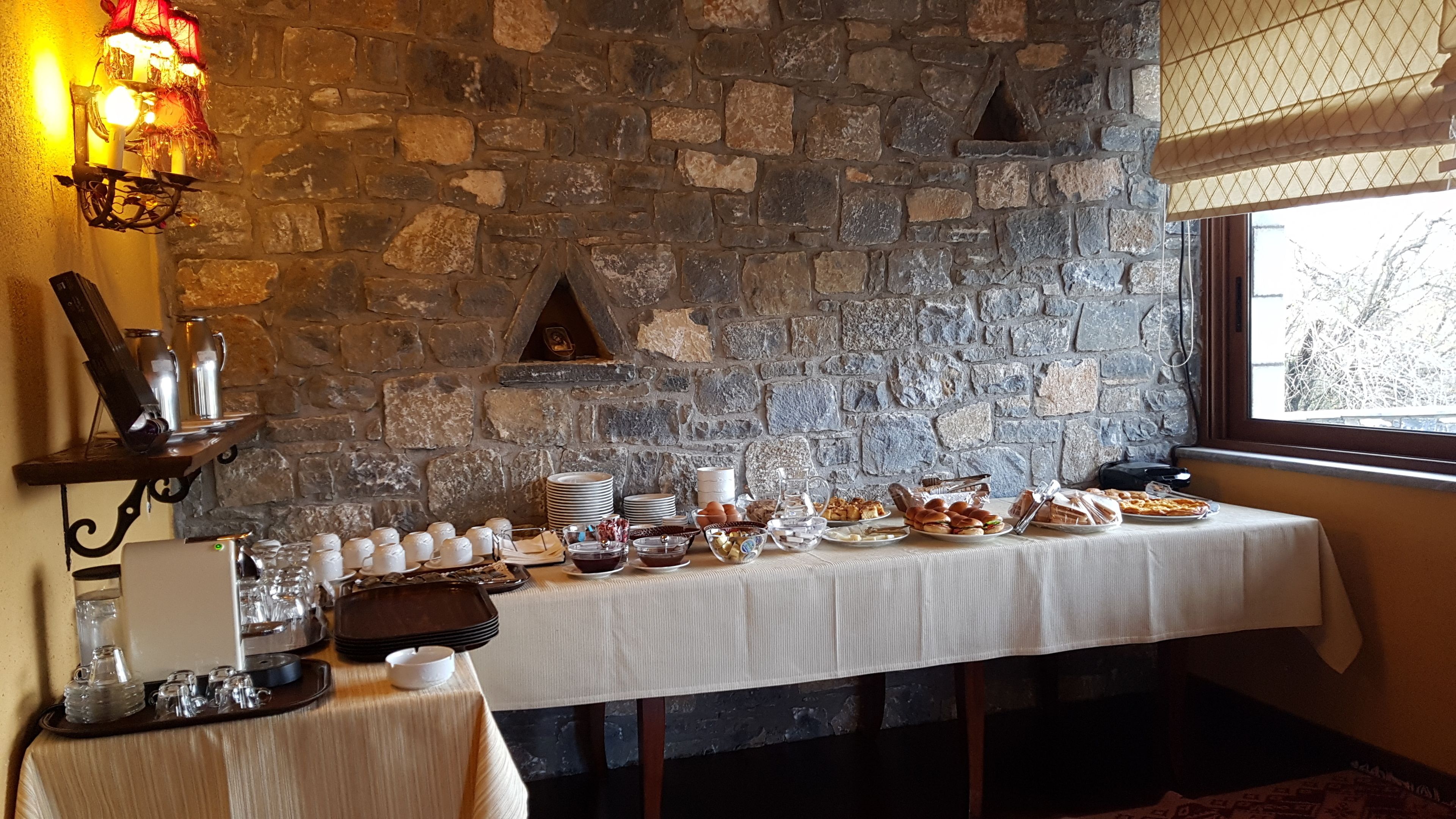 Un bufé de desayuno con diversos alimentos y bebidas, con un fondo de pared de piedra.
