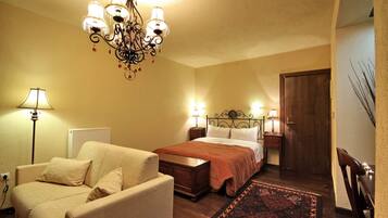 A bedroom with a bed, two bedside tables with lamps, a wooden dresser, a chair, and a chandelier.