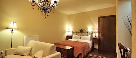 Un dormitorio con una cama, dos mesitas de noche con lámparas, un aparador de madera, una silla y una araña.