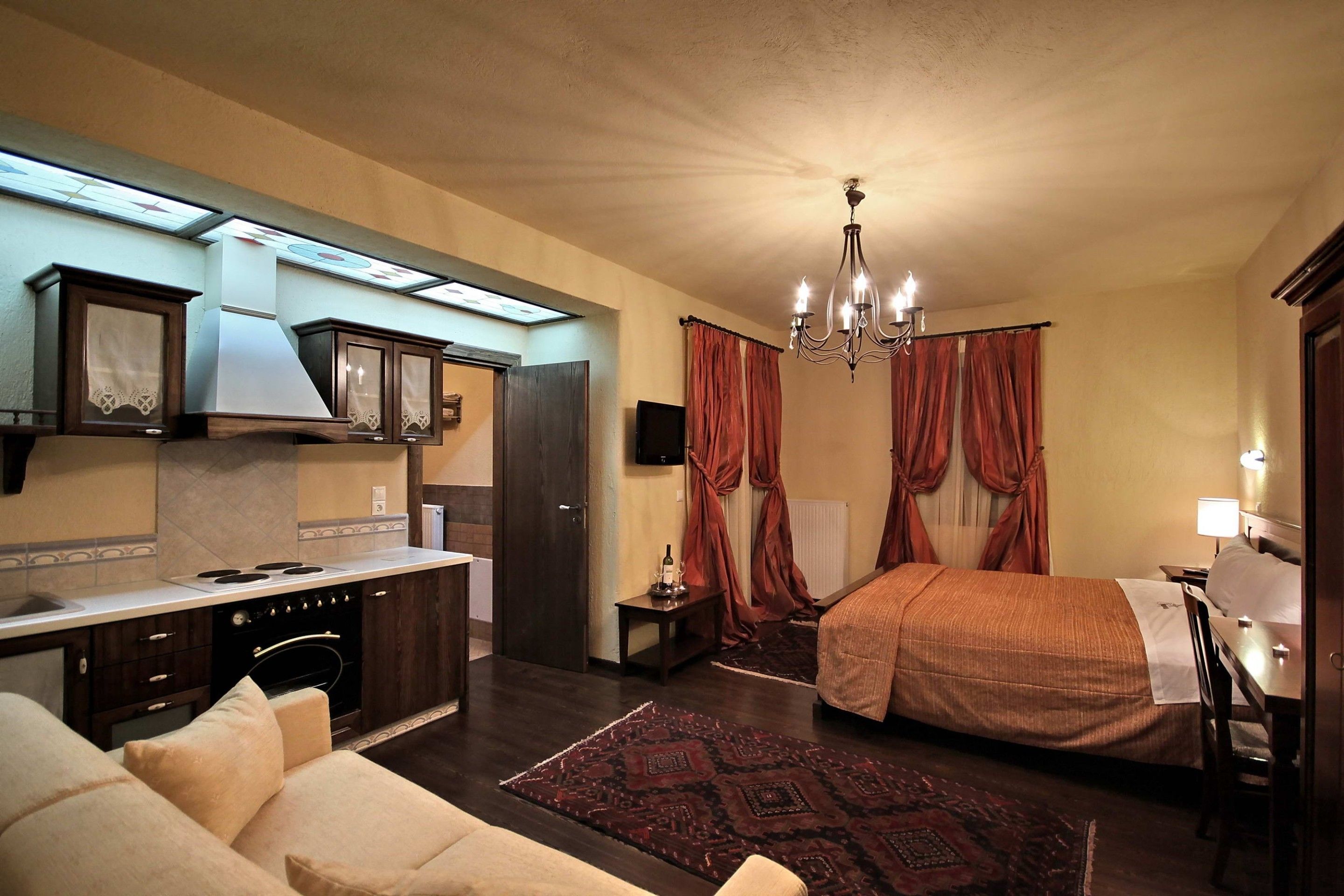 Een compacte hotelkamer met kitchenette, een bed, een slaapbank, een kroonluchter en een televisie.
