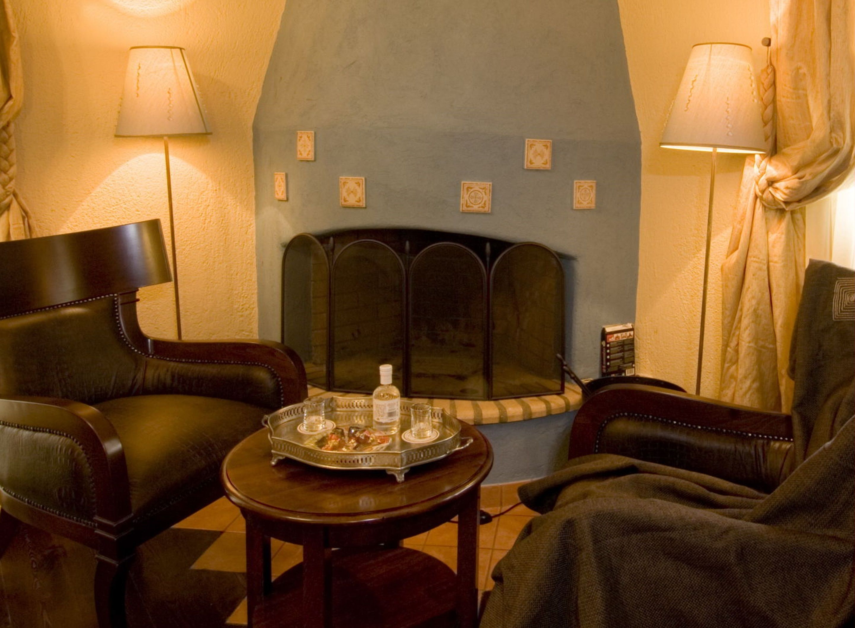 A cozy room with a fireplace, leather chairs, a small table with a tray, and lamps.