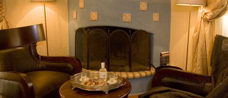 A cozy room with a fireplace, leather chairs, a small table with a tray, and lamps.