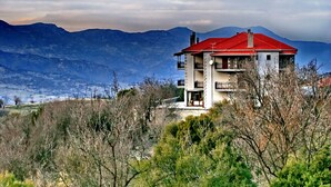 Una casa de dos pisos con techo rojo, rodeada de montañas y árboles.