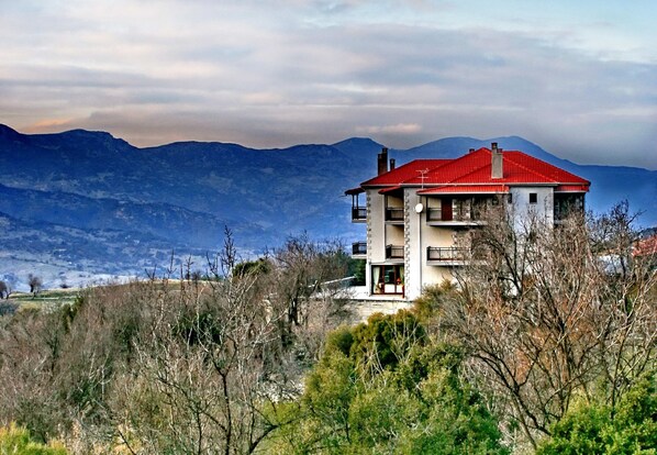 A two-story house with a red roof, surrounded by mountains and trees.