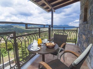 A balcony with a table set for breakfast, including a jug of orange juice, a cup, and a basket of bread. - Aiora Luxury Suites (Gortynia)