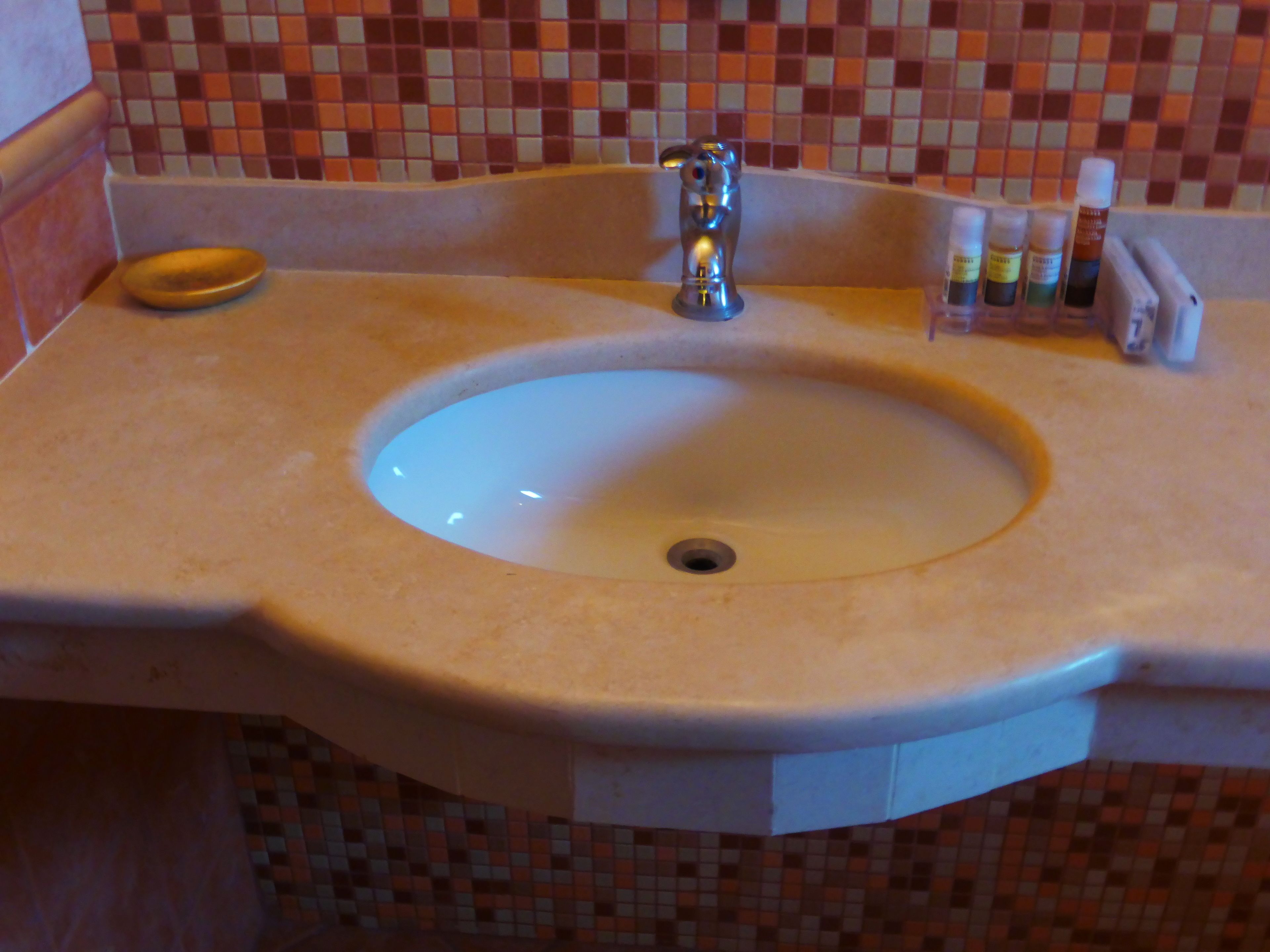 A bathroom sink with a mirror, a soap dish, and a row of toiletries.