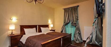 Una cama doble con cabecera de madera, dos mesitas de noche con lámparas, un candelabro y una alfombra roja estampada.