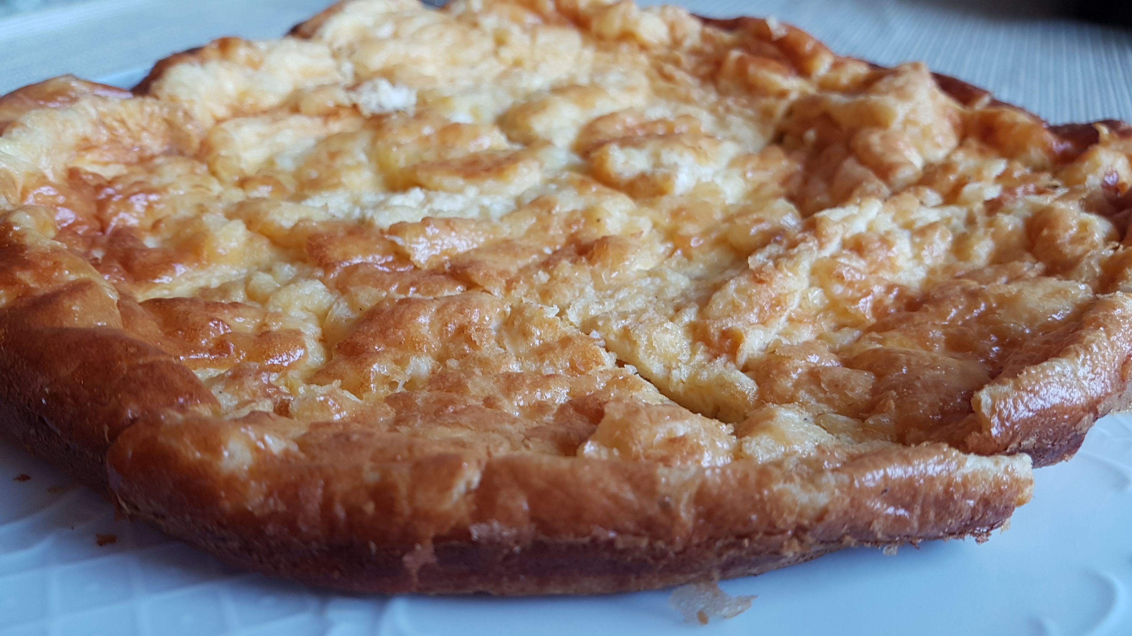 A close-up of a baked dish with a golden-brown crust, possibly a savory pie or tart, on a white plate.