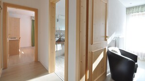 A room with a wooden floor, a black chair, and a view of a bathroom with a sink and towel rack. - Hotel Traube – Stelvio (Stelvio)