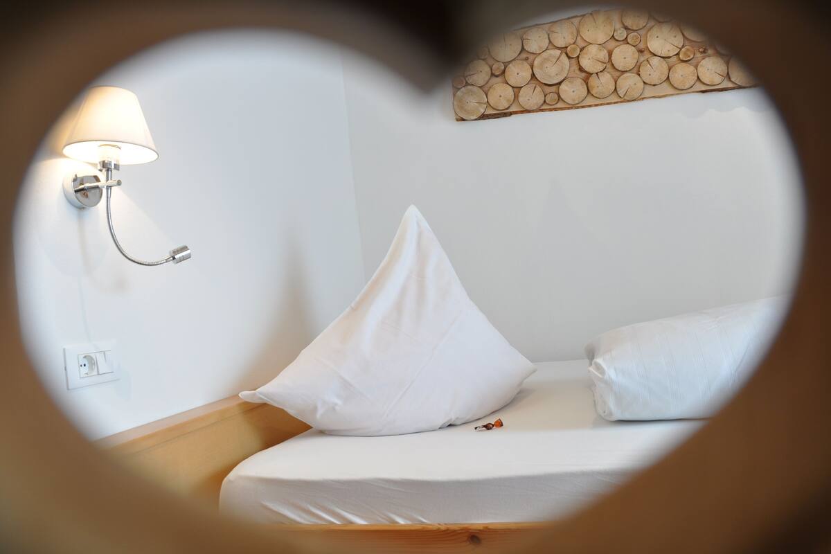 A hotel room with a bed, a wall-mounted lamp, and a wooden headboard.