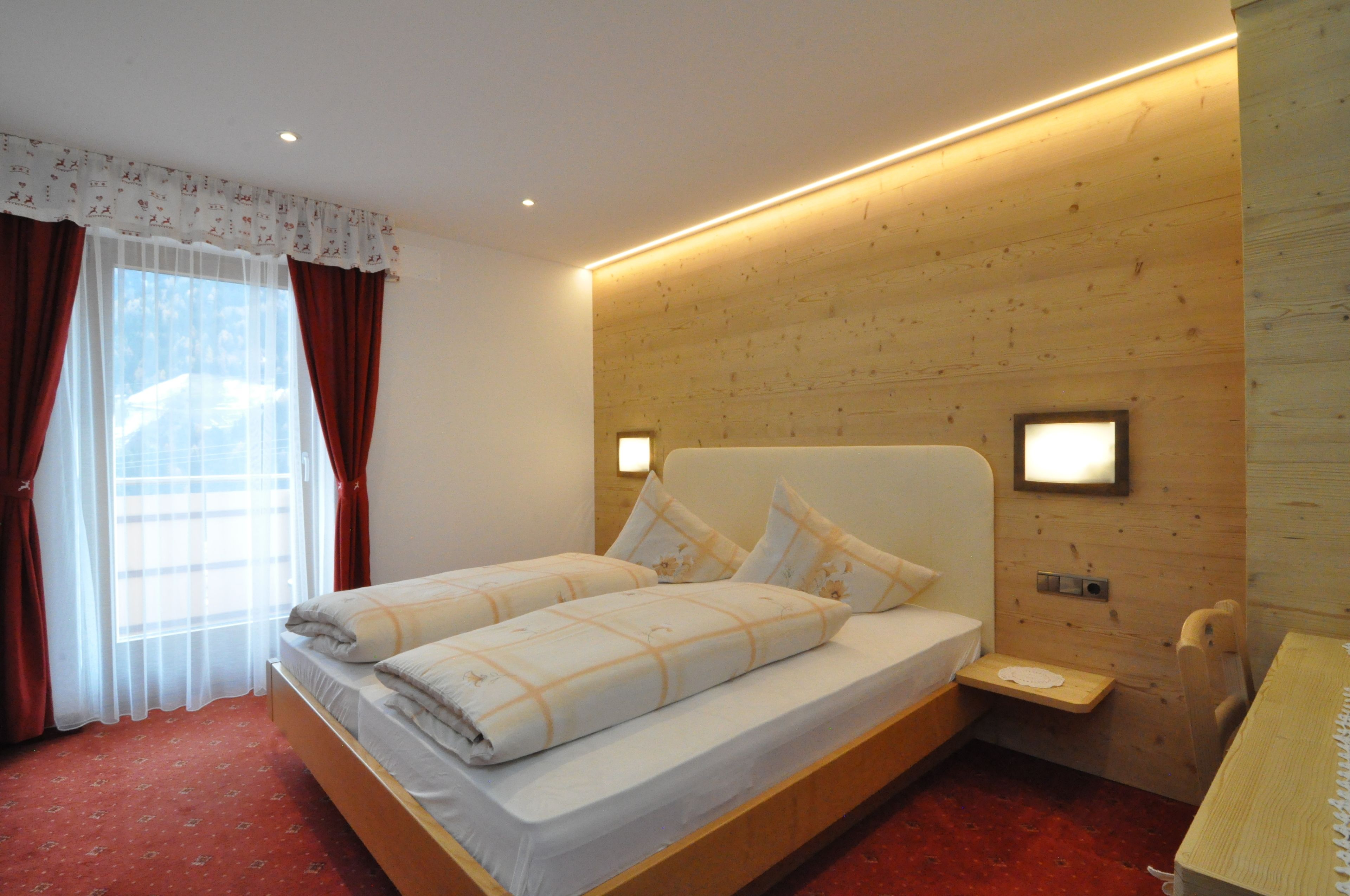 A hotel room with a wooden headboard, a bed with white bedding, a bedside table, and a small bedside lamp.