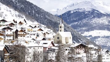 Uma aldeia coberta de neve com arquitetura alpina tradicional, incluindo casas de madeira e uma igreja com um campanário.